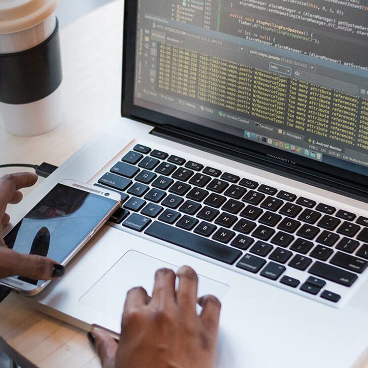 Bilde av en laptop og mobil og noen hender som skriver på laptopen