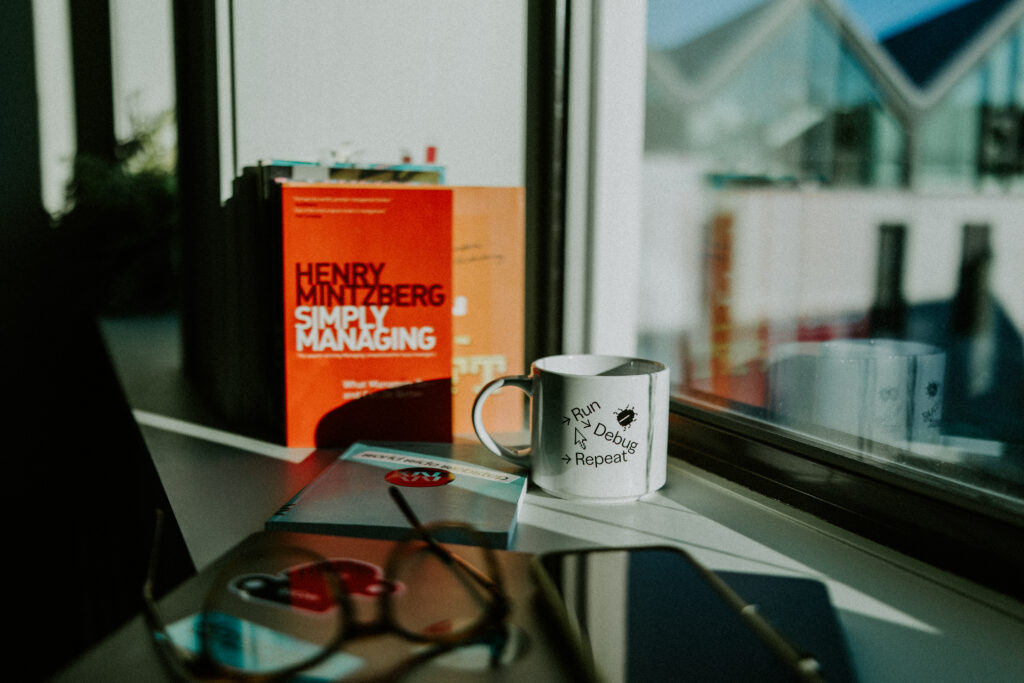 Kaffekopp med teksten «Run, Debug, Repeat» på et skrivebord hos Webstep.