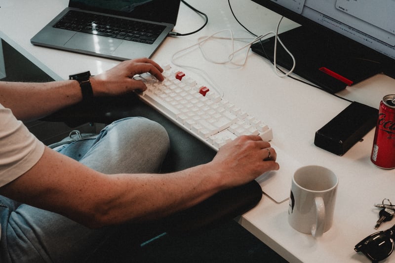 Person arbeider ved en datamaskin med tastatur, mus og skjerm på en kontorarbeidsplass.